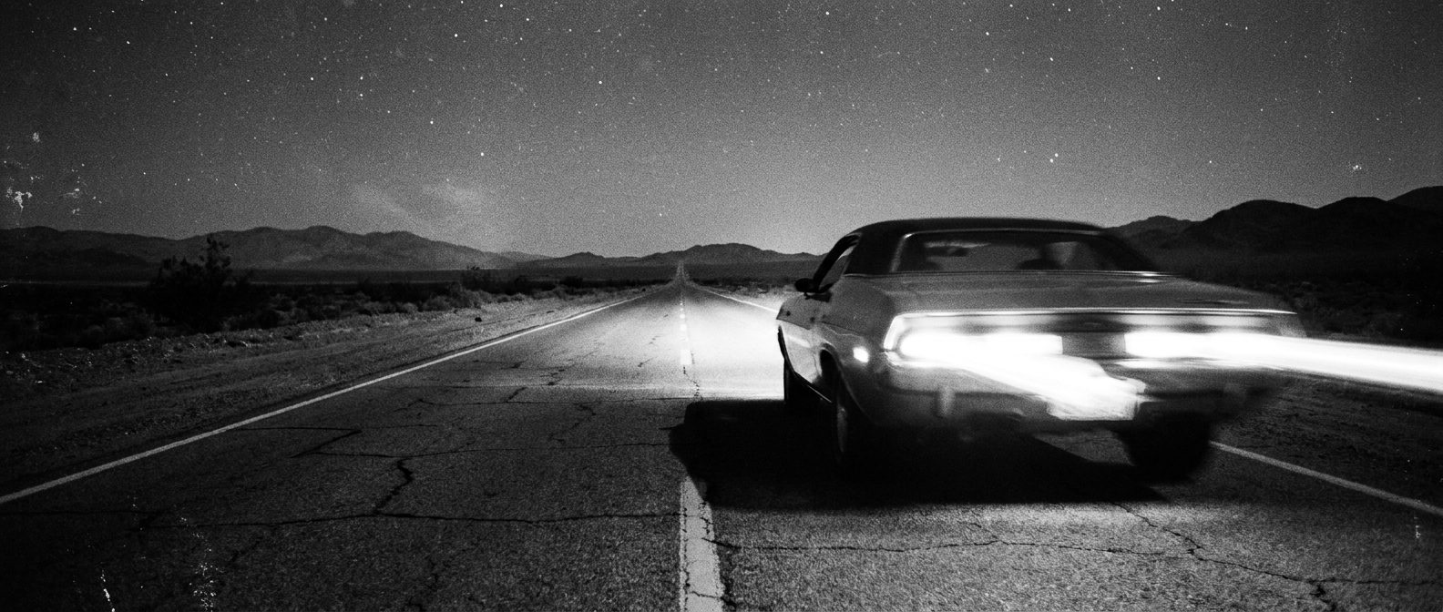 Classic car tail lights streaking down a night highway, black and white